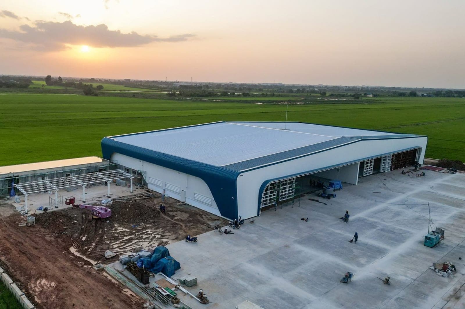 The terminal and hangar at Guardian Blue Airport at sunset, seen from the air, with rice fields beyond.