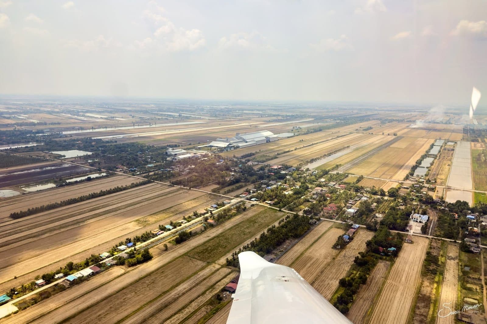 The airfield and surrounding farmland seen from the air, with an aircraft wingtip in frame.